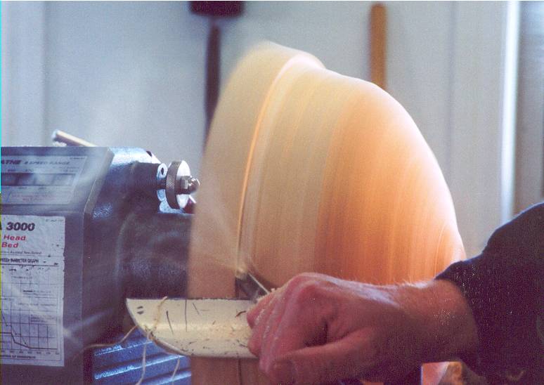 Turning the outside of a wooden salad bowl on a lathe, tool engaged with the work