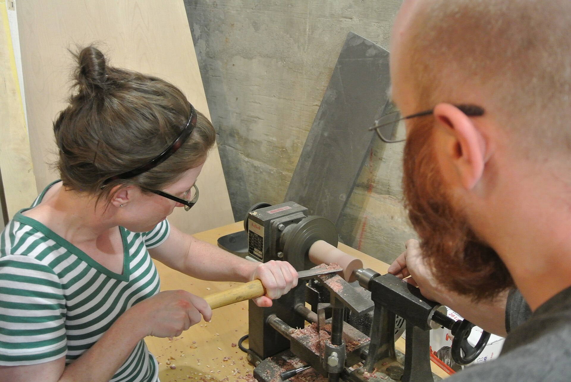 A beginner woodturner making an initial roughing cut on a bowl blank at a workbench lathe