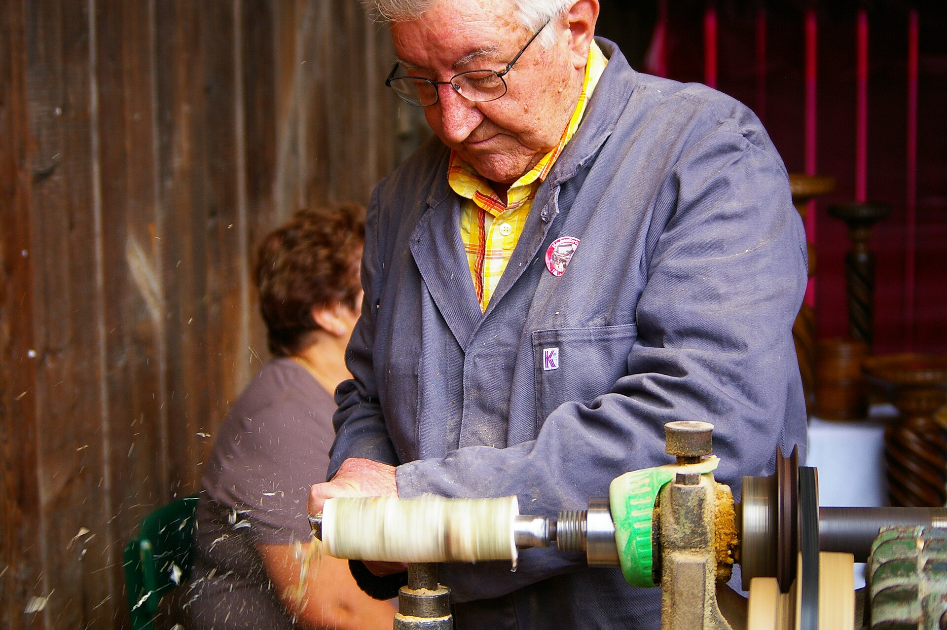 Turner at a traditional wood lathe, shaping a piece on the tool rest with shavings falling