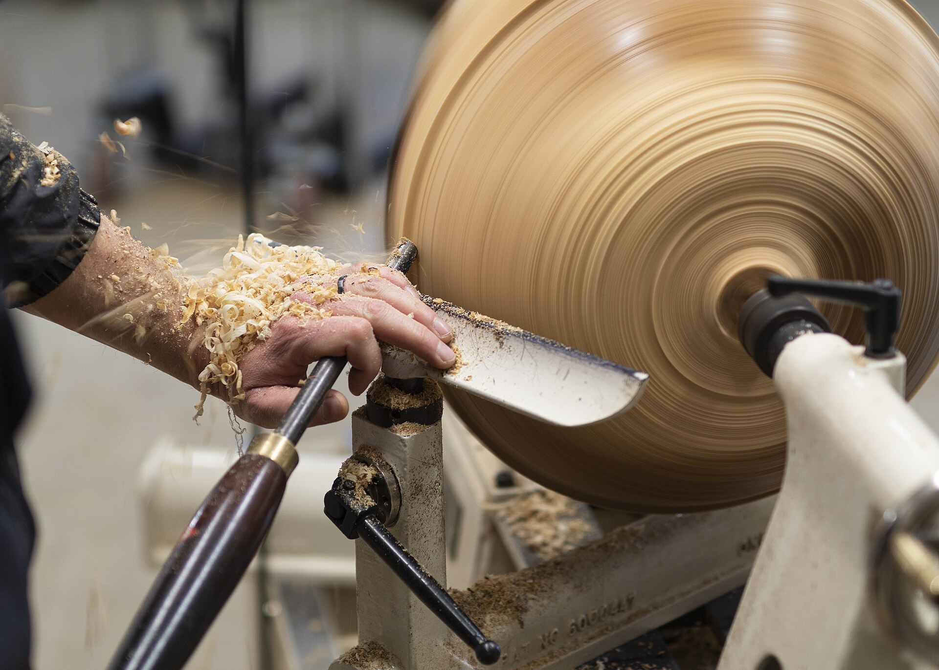 Turner shaping a wooden bowl on a lathe, tool riding the rest with shavings curling