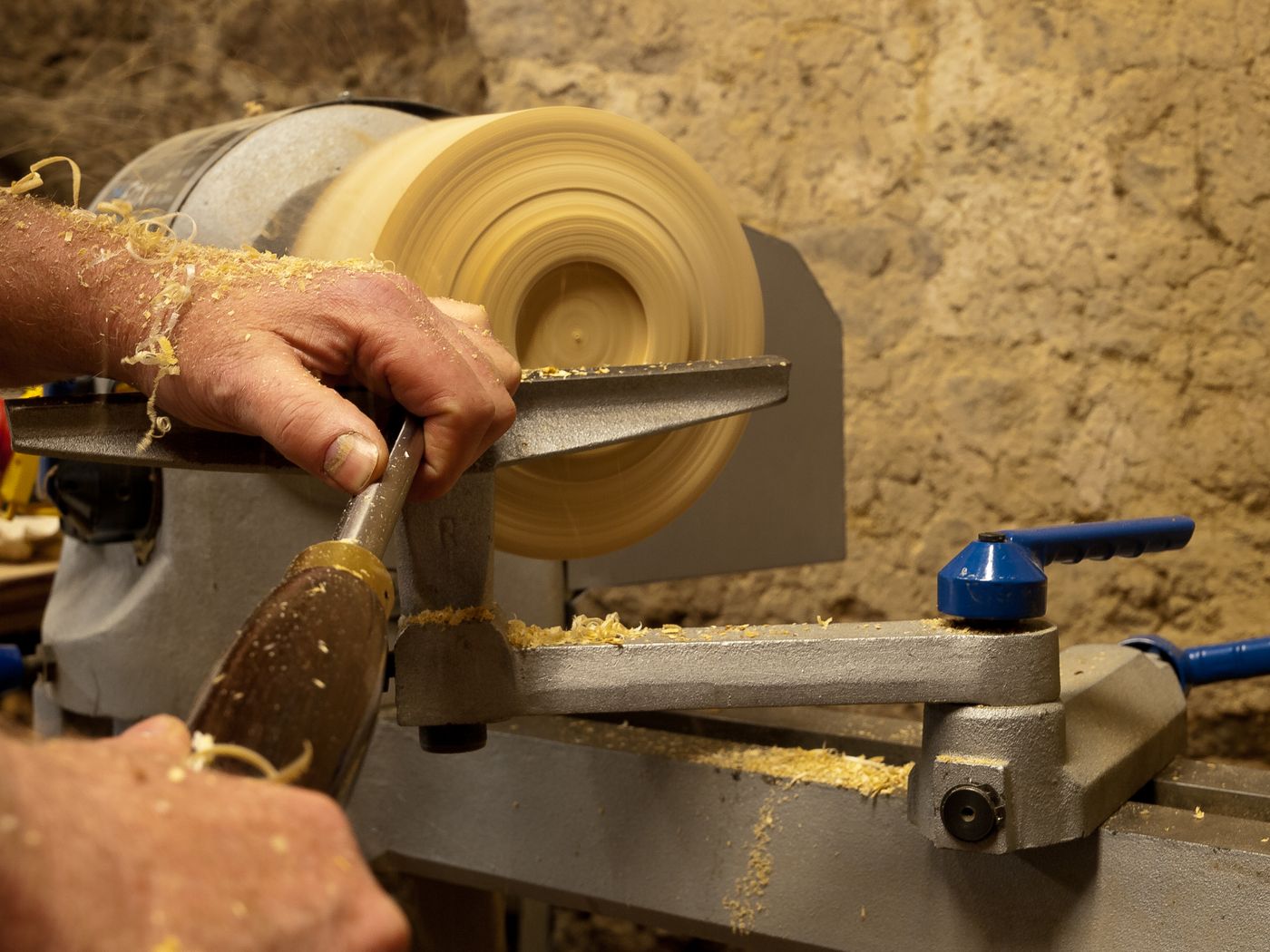 A woodturner works at a lathe in a rustic workshop, shaping a piece with care