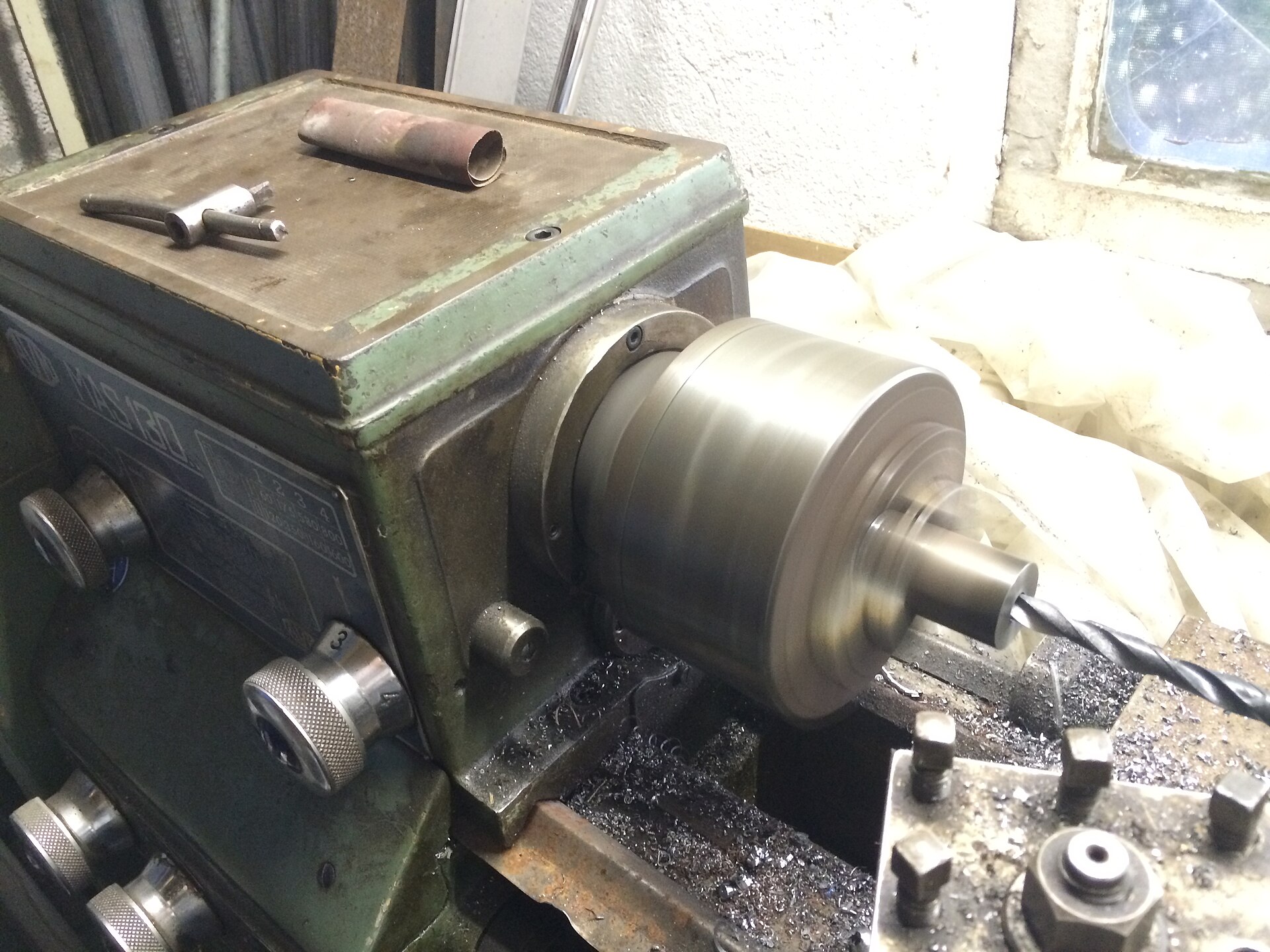 Turner at work on a wood lathe in a workshop, viewed from the side