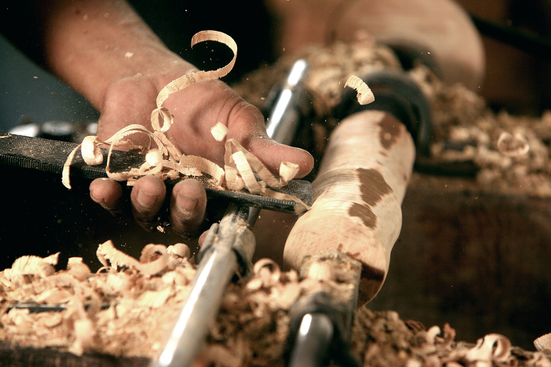 A turner at a floor lathe in a well-lit shop, the lathe mounted directly on the floor with tools to the left