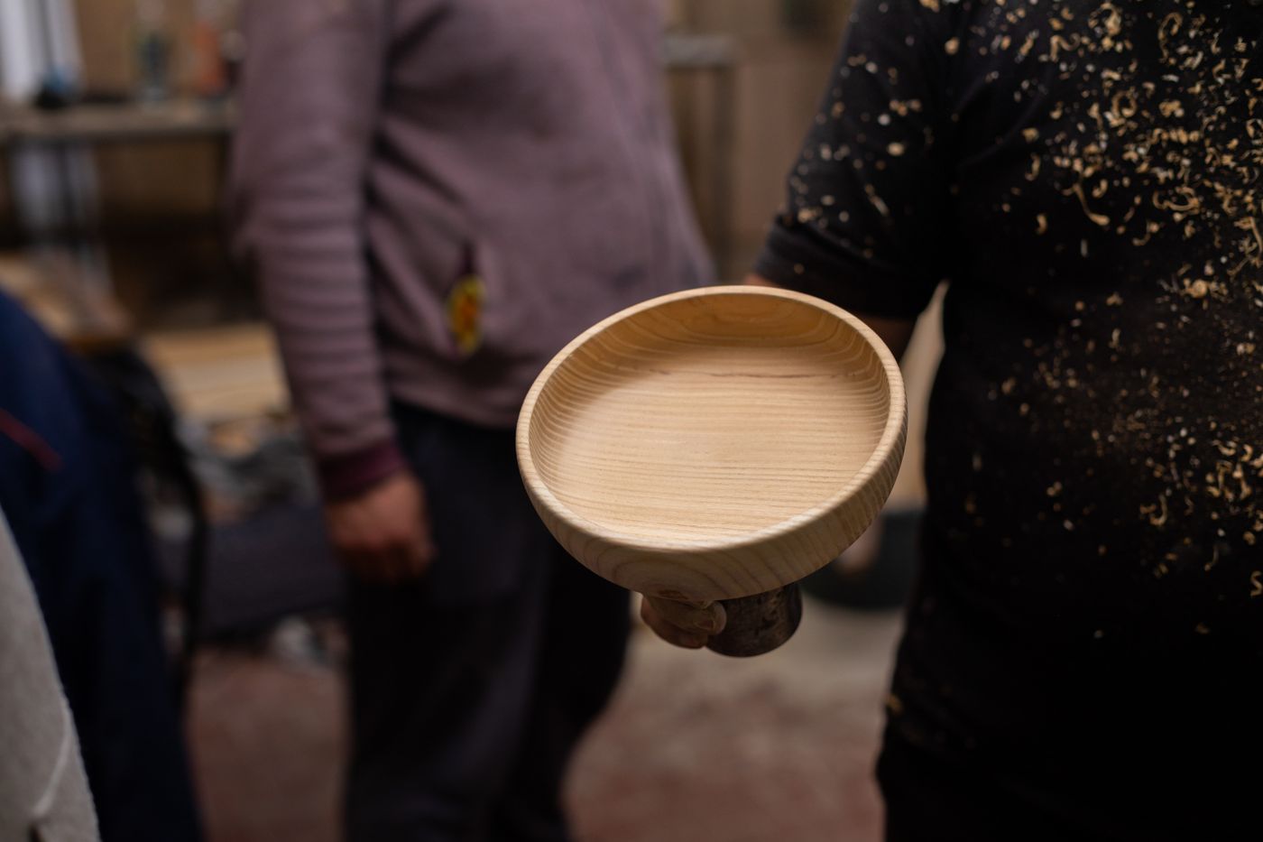 Handmade turned wooden bowl held in a craftsman's hands in a workshop setting
