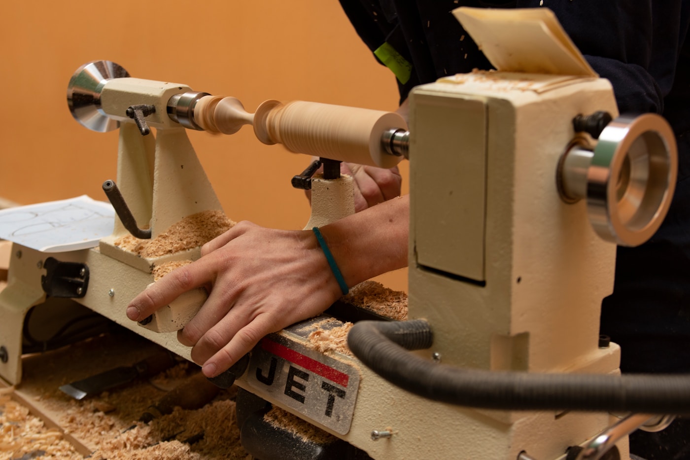 A woodworker shaping a piece on a lathe, wood shavings on the floor of the shop