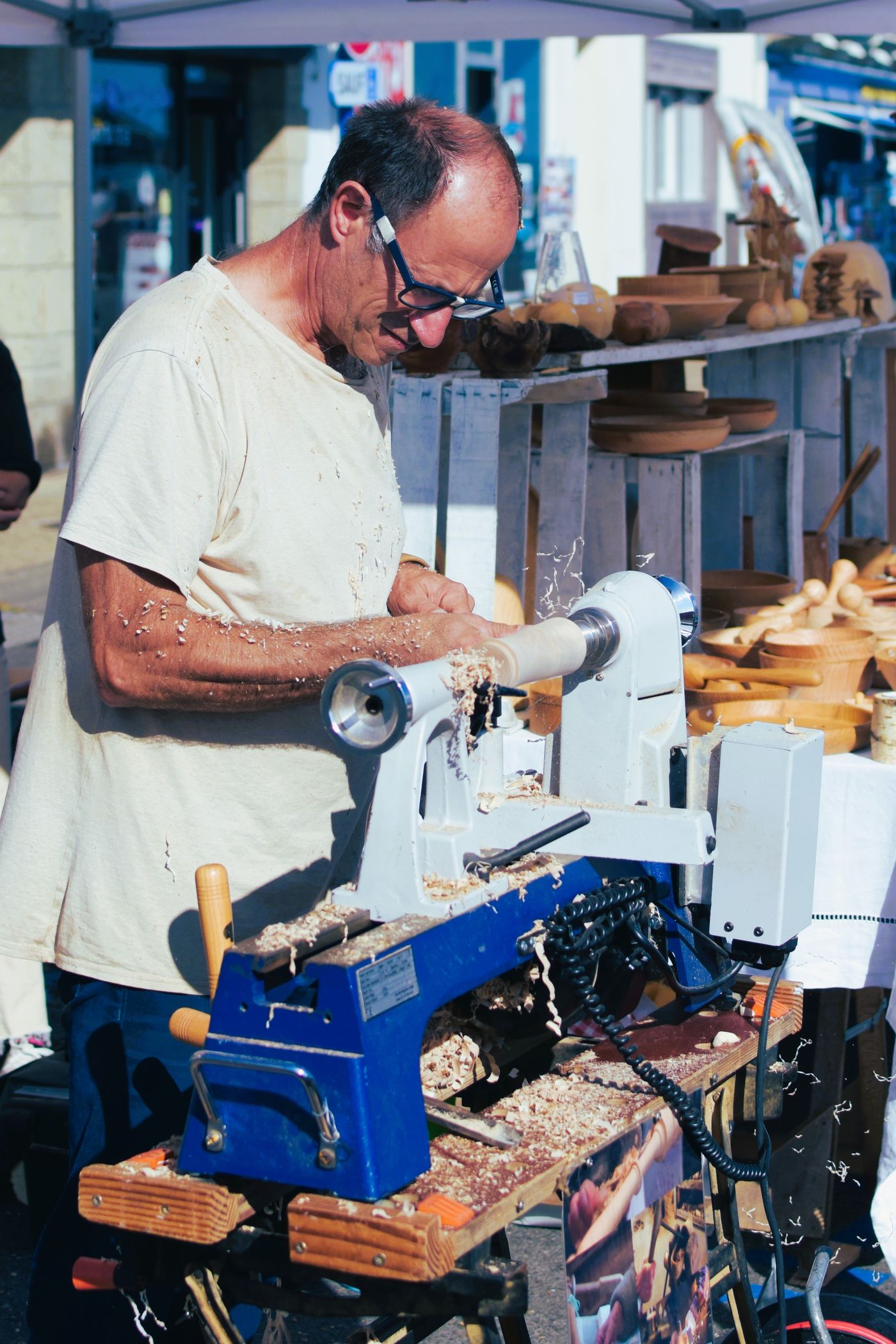 Turner demonstrating bowl turning at an outdoor craft market in Camaret-sur-Mer, France, with finished bowls displayed for sale