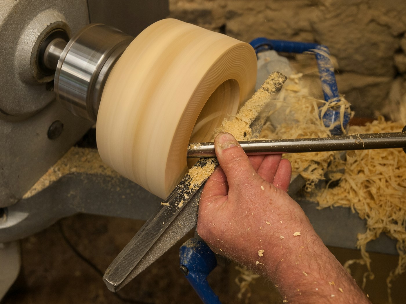 A craftsman shapes wood on a lathe in a bright workshop, focused on the work