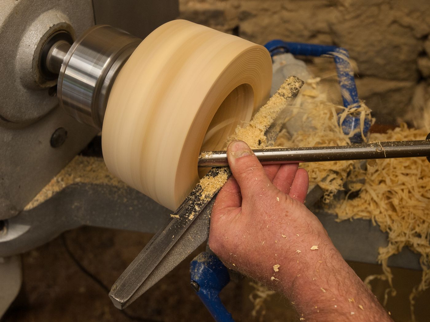 A woodturner at work at a lathe in a workshop, shaping a piece